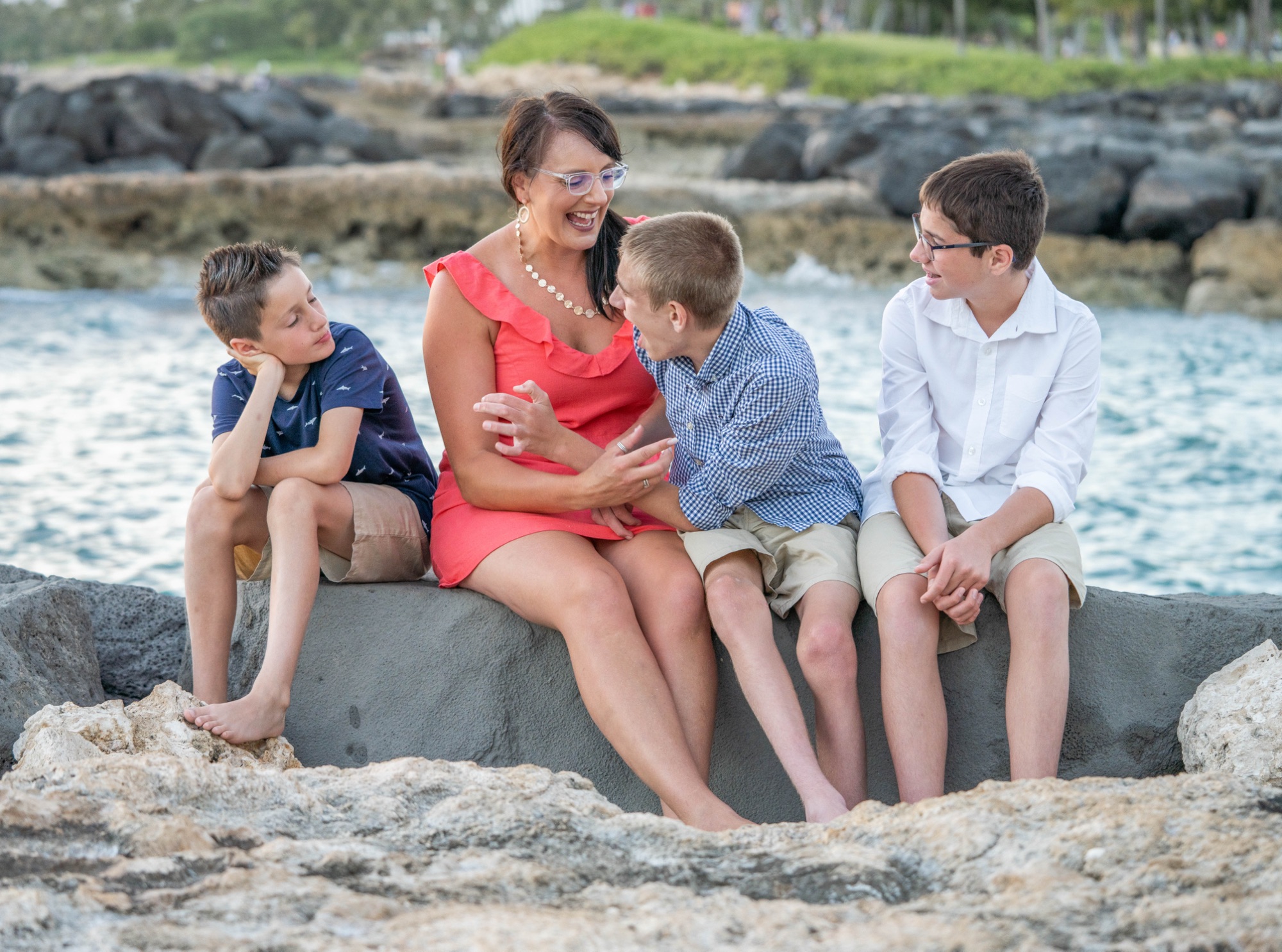 Gina and her three sons sit together on rocks beside the water.